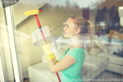 Image of happy woman in gloves cleaning window with sponge