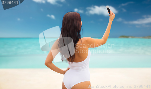 Image of young woman taking selfie with smartphone on beach