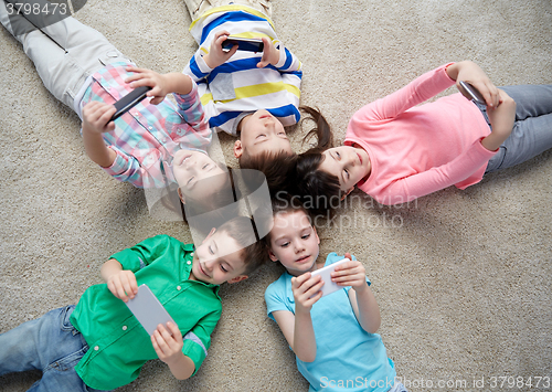 Image of happy children with smartphones lying on floor