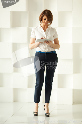 Image of Businesswoman standing against white wall while looking at tablet