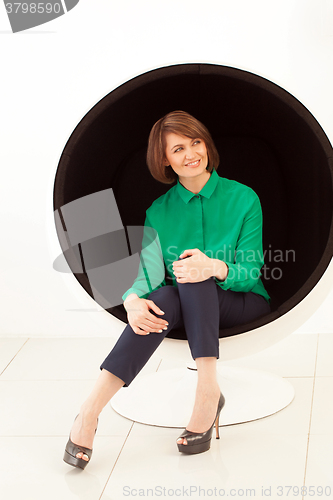 Image of Red haired smiling woman looking away while sitting on modern chair