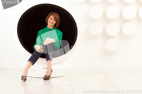Image of Attractive woman sitting on spherical chair with hands on knees
