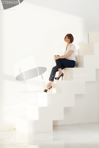 Image of Elegant adult woman smiling while sitting on steps