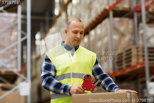 Image of man in safety vest packing box at warehouse