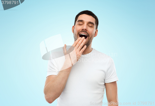 Image of tired sleepy yawning man over blue background