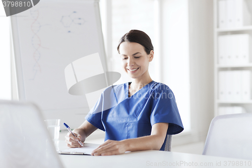 Image of happy female doctor or nurse writing to clipboard