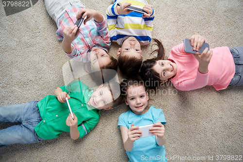 Image of happy children with smartphones lying on floor