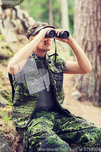 Image of young soldier or hunter with binocular in forest