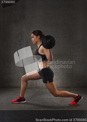 Image of young woman flexing muscles with barbell in gym