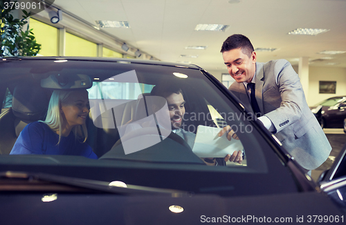 Image of happy couple with car dealer in auto show or salon