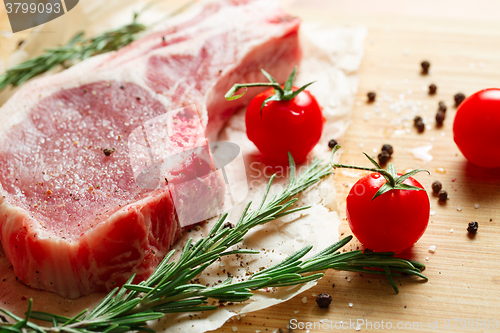 Image of Pieces of crude meat with rosemary and tomatoes.