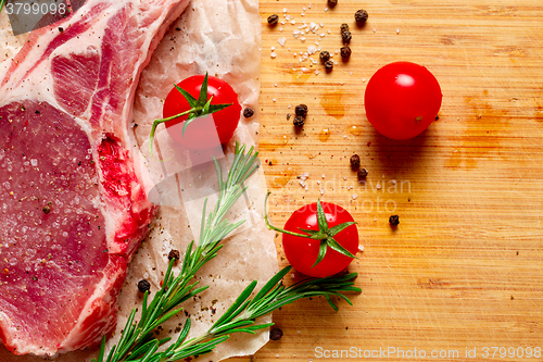 Image of Pieces of crude meat with rosemary and tomatoes.