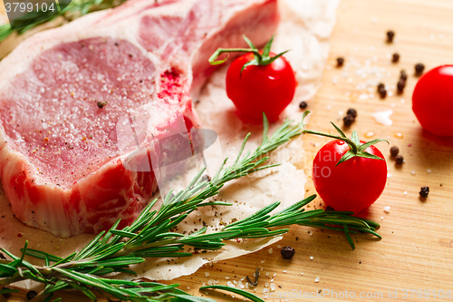 Image of Pieces of crude meat with rosemary and tomatoes.