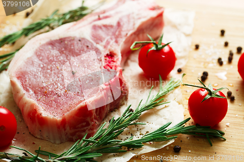 Image of Pieces of crude meat with rosemary and tomatoes.