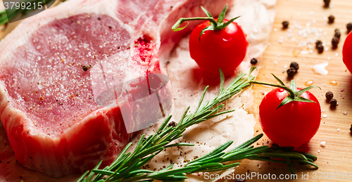 Image of Pieces of crude meat with rosemary and tomatoes.