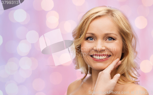 Image of smiling woman with bare shoulders touching face