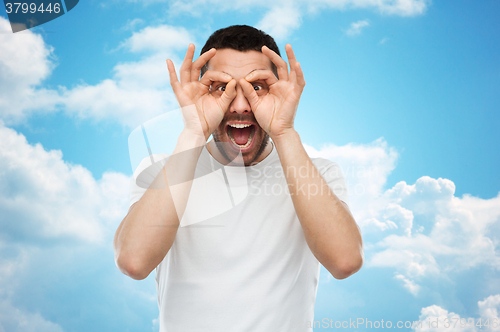 Image of man making finger glasses over blue sky