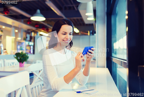 Image of smiling woman with smartphone at cafe