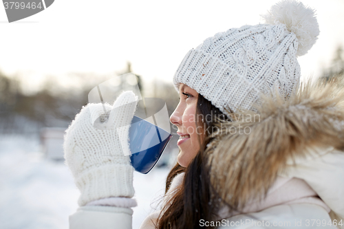 Image of happy young woman with tea cup outdoors in winter