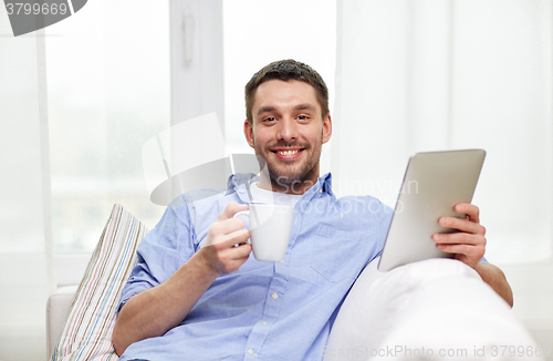 Image of smiling man with tablet pc drinking tea at home