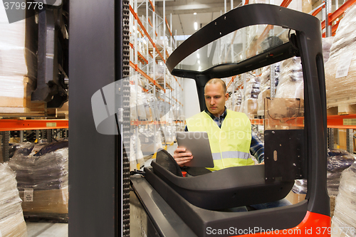 Image of man with tablet pc operating forklift at warehouse