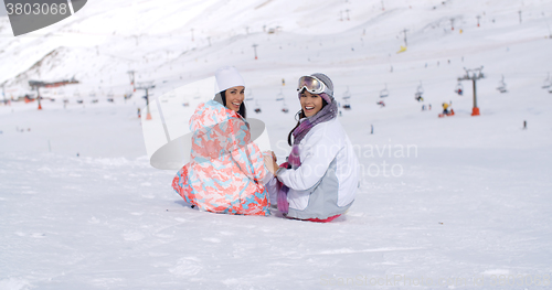 Image of Two young women sitting in snow at a ski resort