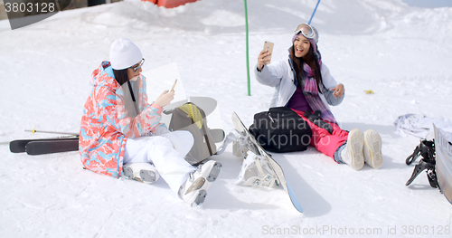 Image of Young female friends relaxing with snowboards