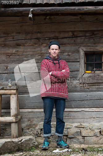 Image of young hipster in front of wooden house