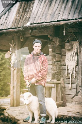 Image of young hipster with dog in front of wooden house