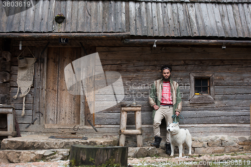 Image of hipster with dog in front of wooden house