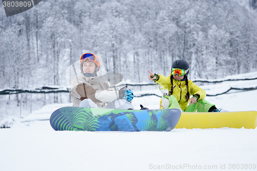 Image of Two snowboarders - men and women sitting in the mountains