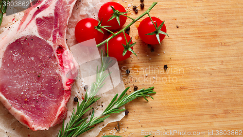 Image of Pieces of crude meat with rosemary and tomatoes.