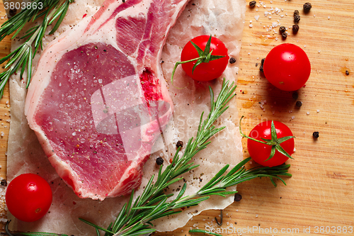 Image of Pieces of crude meat with rosemary and tomatoes.