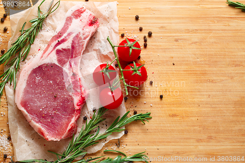 Image of Pieces of crude meat with rosemary and tomatoes.