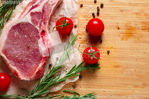 Image of Pieces of crude meat with rosemary and tomatoes.