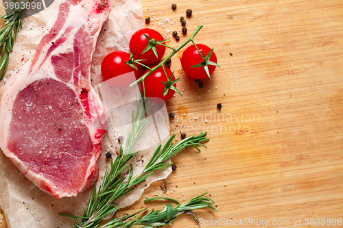 Image of Pieces of crude meat with rosemary and tomatoes.