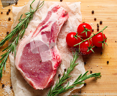 Image of Pieces of crude meat with rosemary and tomatoes.