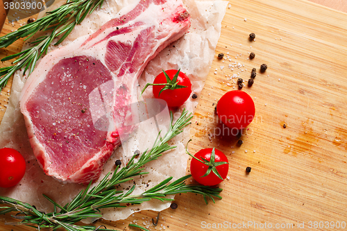 Image of Pieces of crude meat with rosemary and tomatoes.