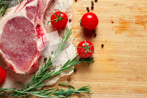 Image of Pieces of crude meat with rosemary and tomatoes.