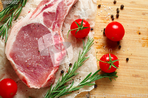 Image of Pieces of crude meat with rosemary and tomatoes.