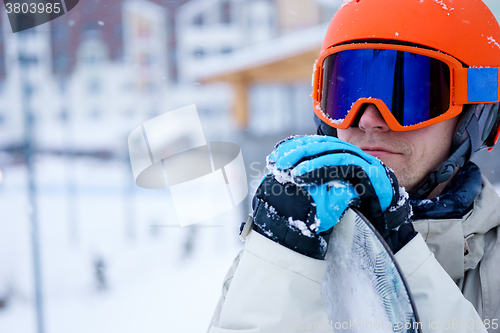 Image of Man snowboarder wearing orange helmet, grey jacket, black and blue gloves standing with snowboard