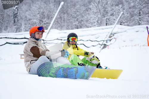 Image of Two snowboarders - men and women sitting in the mountains