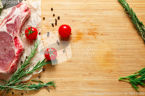 Image of Pieces of crude meat with rosemary and tomatoes.