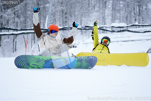 Image of Two snowboarders - men and women sitting in the mountains