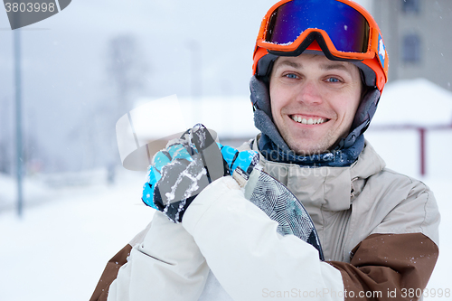 Image of Man snowboarder wearing orange helmet, grey jacket, black and blue gloves standing with snowboard
