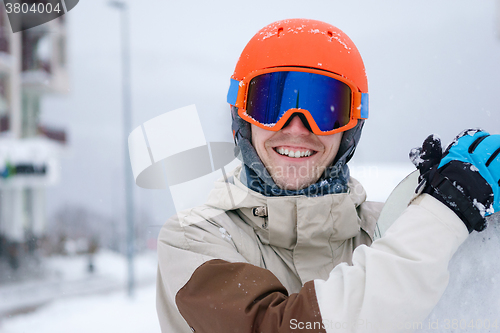 Image of Man snowboarder wearing orange helmet, grey jacket, black and blue gloves standing with snowboard