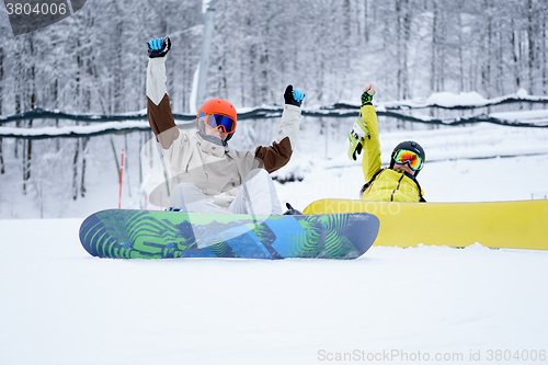 Image of Two snowboarders - men and women sitting in the mountains
