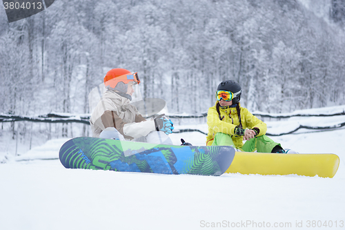 Image of Two snowboarders - men and women sitting in the mountains