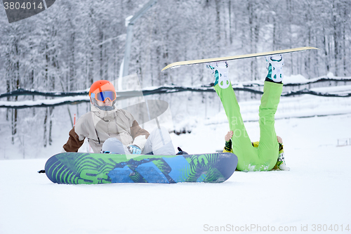 Image of Two snowboarders - men and women sitting in the mountains