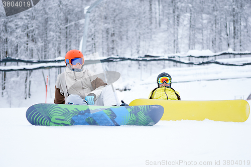 Image of Two snowboarders - men and women sitting in the mountains